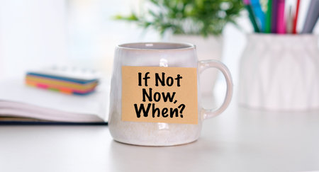 If Not Now, When motivational message on a sticky note attached to a coffee mug on a bright office desk.の写真素材