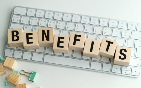 Wooden letters spell BENEFITS on a sleek keyboard. Scattered clips and blocks add playful office charm. Clean desk hints at productivity and workplace value. Ideal for HR, finance