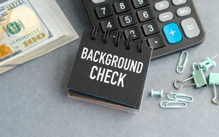Black notepad reads BACKGROUND CHECK. Stacked cash and calculator nearby. Paper clips scattered around desk. Neutral tone, professional feel. Ideal for finance, hiring, or security themes