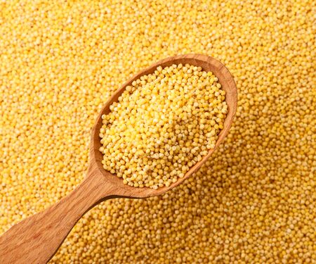 Millet in a wooden spoon close-up on a background of cereals. The view from top