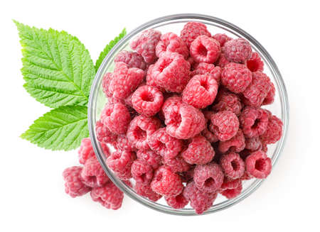 Ripe raspberries with green leaves in a plate close up on a white background. Top view