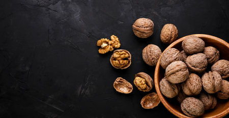 Walnuts in a wooden plate and scattered on a black background. Place for textの写真素材