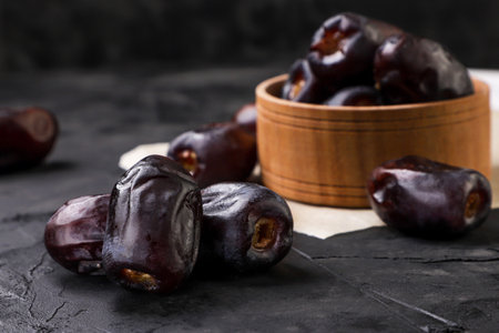 Dates fruit in a wooden plate and a heap close-up on a dark background.の写真素材