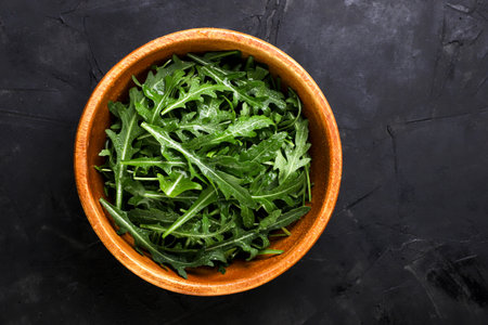 Fresh leaves of arugula in a wooden plate on a dark background. top viewの写真素材