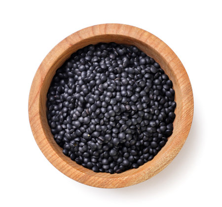 Black lentils in a wooden plate close-up on a white background. View topの写真素材
