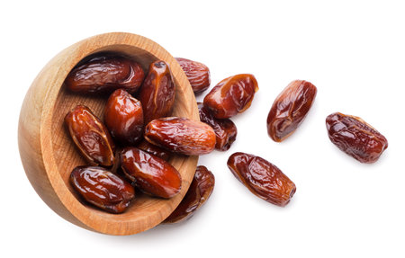 Dates fruits spilled out from a wooden plate close-up on a white background. Top view