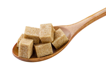 Brown sugar cubes in a wooden spoon close-up on a white background. Isolatedの写真素材