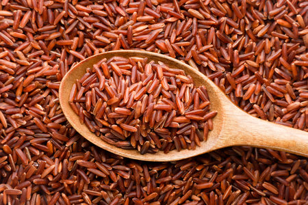 Red rice in a wooden spoon close-up, background. Top viewの写真素材