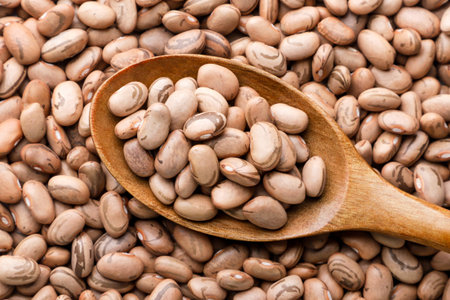 Raw beans in a wooden spoon close up, background. Top view