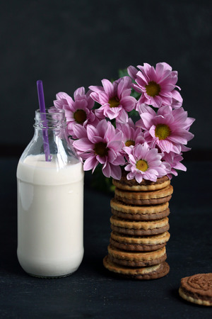 Sweet cookies, bottle of milk and pink flowers for breakfastの写真素材