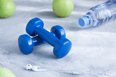 Dumbbells, earphones, apples, bottle of water on gray concrete background. Concept healthy...