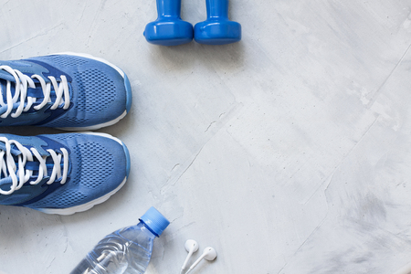 Flat lay sport shoes, bottle of water, dumbbells and earphones on gray concrete background. Concept healthy lifestyle, sport and diet. Focus is only on the sneakers. Sport equipment.の写真素材