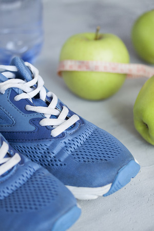 Sport shoes, meter, apples, bottle of water on gray concrete background. Concept healthy lifestyle, sport and diet. Focus is only on the sneakers.の写真素材