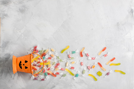 Halloween orange bucket with face, with candies inside and jujube on gray concrete background