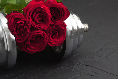 Valentines festive sports background with heavy dumbbell for workout, red rose with 
leaves on black concrete. Concept sport gift for beloved. Horizontal orientation.の写真素材