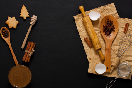 Dark wooden baking background with kitchen tools: rolling pin, wooden spoons, whisk, sieve, spices, honey. Horizontal orientation with copyspace in the middle, top view.の写真素材
