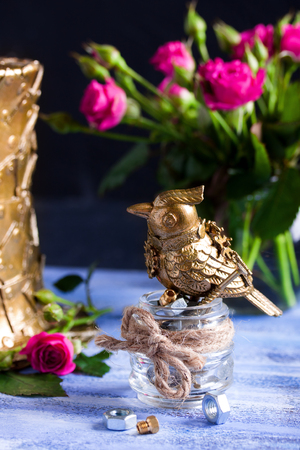 Steampunk bronze bird on glass cup, pink flowers, metallic hat on blue wooden tray.の写真素材