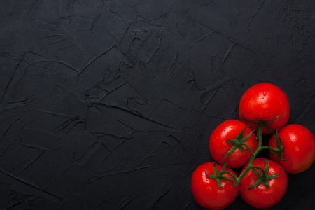 Red fresh large organic tomatoes with green leaves on black concrete background. 
Horizontal orientation, top view, place for copyspace.の写真素材