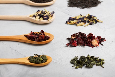 Four wooden spoons with different tea leaves: black, blue, red (hibiscus) and green on grey concrete background. Horizontal orientation, closeup, focus on red tea.の写真素材