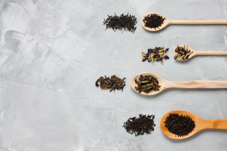 Four wooden spoons with different tea leaves: black, white, blue, green on grey concrete background. Horizontal orientation, top view.の写真素材