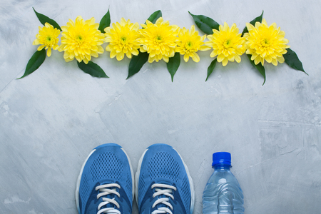 Summer spring flatlay sports composition with blue sneakers, bottle of water 
and yellow chrysanthemum flowers and green leaves on gray concrete background. 
Concept healthy lifestyle, sport and diet in summer, spring. Horizontal 
orientation, top view.の写真素材