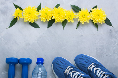 Summer spring flatlay sports composition with blue sneakers, dumbbells, bottle of water and yellow chrysanthemum flowers and green leaves on gray concrete background. Concept healthy lifestyle, sport and diet in summer, spring. Horizontal orientation, topの写真素材