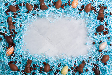 Chocolate easter eggs, rabbits, brown sweets candies on blue cut packing paper. Concrete background,...