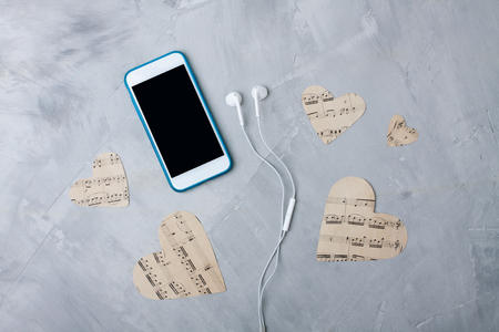 Flatlay composition smartphone or mobile phone, paper hearts, headphones on gray concrete 
background. Music or technology background. Flatlay, top view.の写真素材