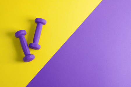 Sport flat lay composition with purple dumbbells on yellow and purple paper background. Top view, horizontal orientation.の写真素材