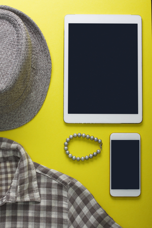 Women's flat lay clothes gray hat, shirt in a box, pearl bracelet, tablet and mobile phone mockup on a yellow 


background. Fashion blog, clothing, shopping, application concept, top view.の写真素材