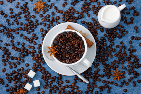 Cup of coffee with seeds, milk in a white milk jug, sugar, spoon, cinnamon and anis on blue background. Horizontal  

orientation, top view.の写真素材