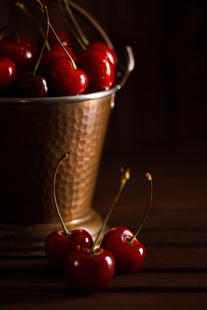 Fresh red cherries in copper bucket on dark wooden background. Summer, 


harvest, vegan, vegetarian, raw food concept. Vertical orientation, macro, 


closeup, place for copy space.の写真素材