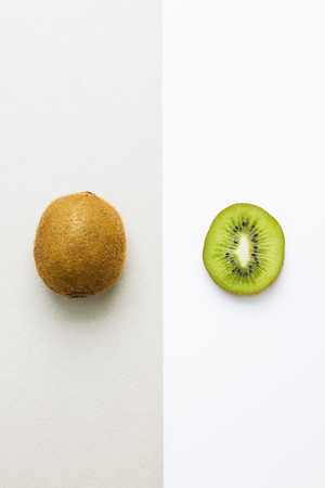 Fresh kiwi whole fruit on grey background and kiwi slice on white background. Creative layout, food concept, flat lay, top view, vertical orientation.の写真素材