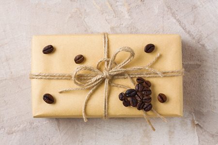 Craft gift box with twine and coffee beans heart shape decoration on beige concrete background, close up. Gift decor idea for coffee lovers. Horizontal orientation, top view, flat lay.の写真素材