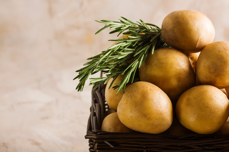 Wooden basket with potatoes and rosemary. Concept vegetables delivery, vegetarian vegan cooking, growing of ecological vegetables. Horizontal orientation, place for copyspace, beige background.の写真素材