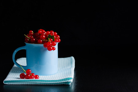 Redcurrant pile (ribes rubrum) in blue cup on blue napkin, dark wooden background. Cooking...