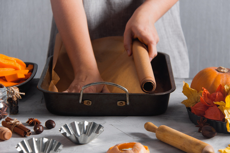 Woman lays out baking paper in iron form, cooking baking. Autumn time, pumpkins, physalis, 


yellow dry leaves, spices, cinnamon, anise, cloves, kitchen tools, wooden rolling, pin, 


nutmegs.の写真素材