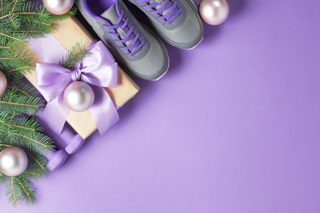 Christmas sport flat lay composition gray shoes, purple dumbbells, craft gift box with lilac bow, spruce tree branches on violet background. Top view, horizontal orientation.の写真素材