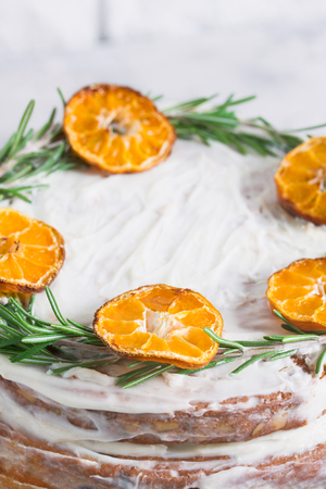 Cake on glass stand decorated with rosemary and dried mandarin slices on grey concrete white brick wall background. Close up, vertical orientation.の写真素材