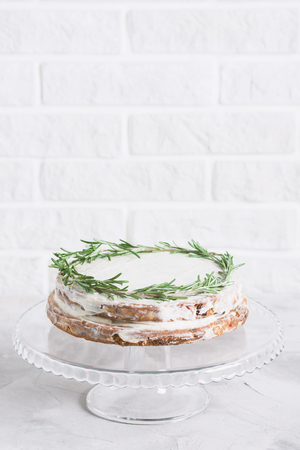Cake on glass stand decorated with sprigs of rosemary on grey concrete white brick wall background. Vertical orientation, place for copy space.の写真素材