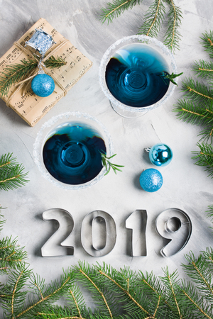 New year composition 2019 letters, martini drink with rosemary and sugar decoration, fir-trees, craft gift box, balls, in blue colors gray concrete background. Winter holiday, Christmas party concept.の写真素材