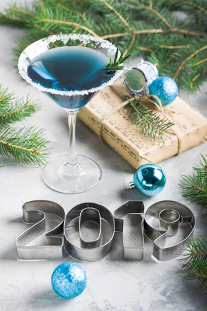 New year composition 2019 letters, martini drink with rosemary and sugar decoration, fir-trees, craft gift box, balls, in blue colors gray concrete background. Winter holiday, Christmas party concept.の写真素材