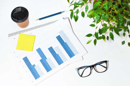 an economists workplace, an office desk with glasses, graphs, a pen and a glass of coffeeの写真素材