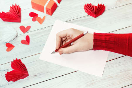 a girl writes a congratulatory love letter on a bright table with red symbols of love and a giftの写真素材