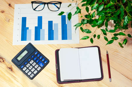 blank notebook with pen, calculator, glasses and graphics on a contemporary workplaceの写真素材