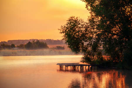 sunrise on the lake with fog in the village.View of the wooden bridgeの写真素材