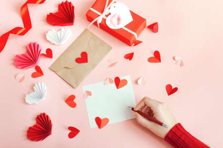 Valentines Day, a girl writes a love message on a pink background with paper hearts and a giftの写真素材