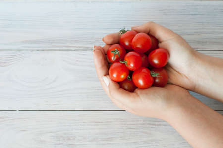 Young girls hands hold cherry tomatoes on a wooden backgroundの写真素材
