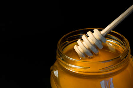 fresh honey is poured into a transparent jar on a black backgroundの写真素材
