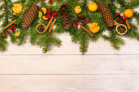 Christmas card, spruce branches with cones on a wooden light background decorated with tangerines. Top viewの写真素材